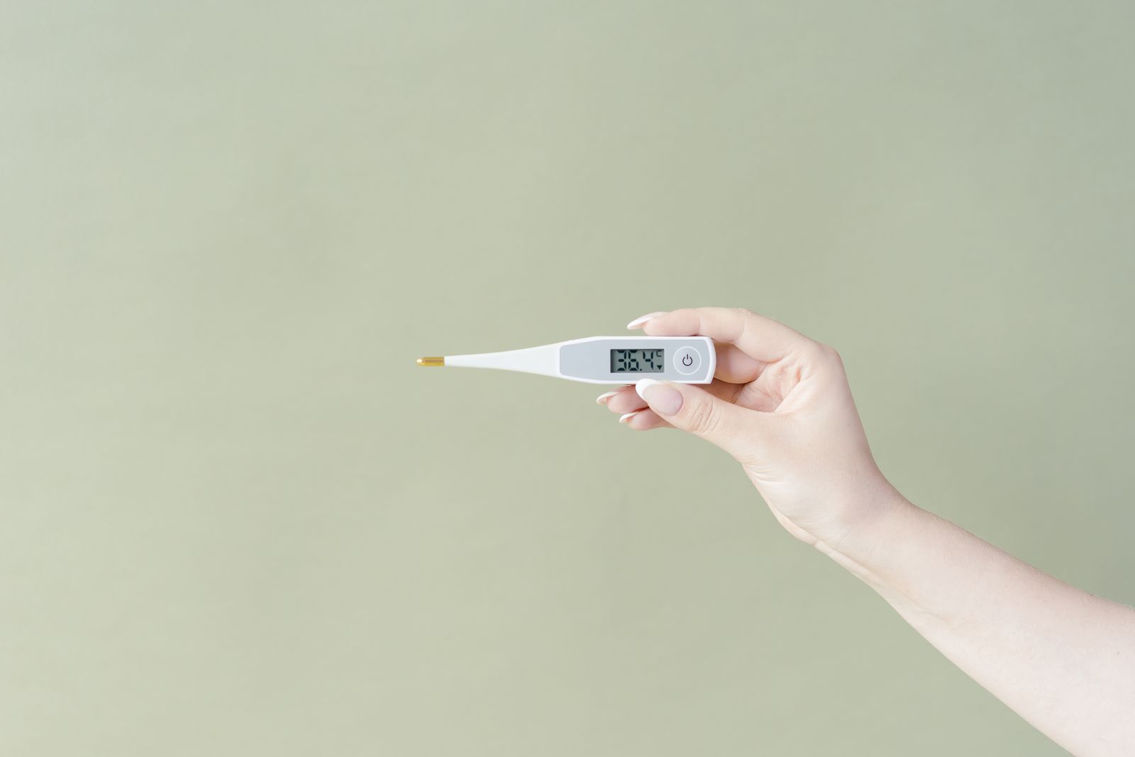Une main tient un thermomètre électronique devant un mur vert pâle