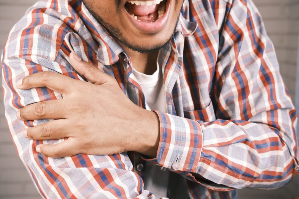 Un homme en chemise à carreaux porte la main à son épaule douloureuse