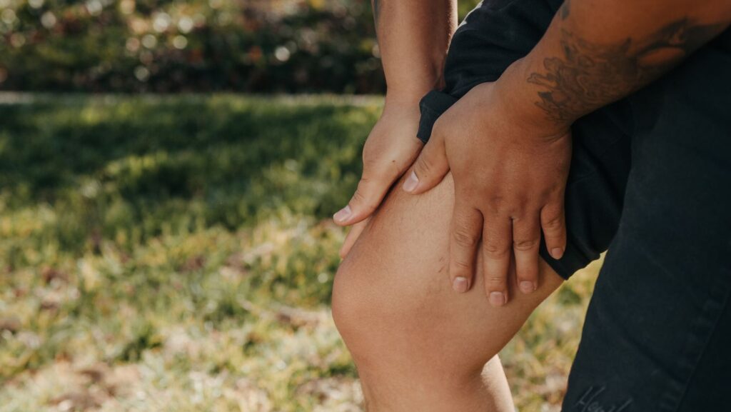 Deux mains posées sur un mollet tendu, en extérieur sur l'herbe
